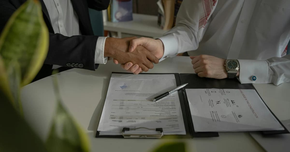Two colleagues shaking hands over employment paperwork after a sponsorship change