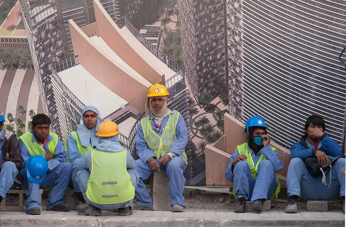 Expatriate workers in hard hats and safety vests sitting at a construction site in West Bay, Doha