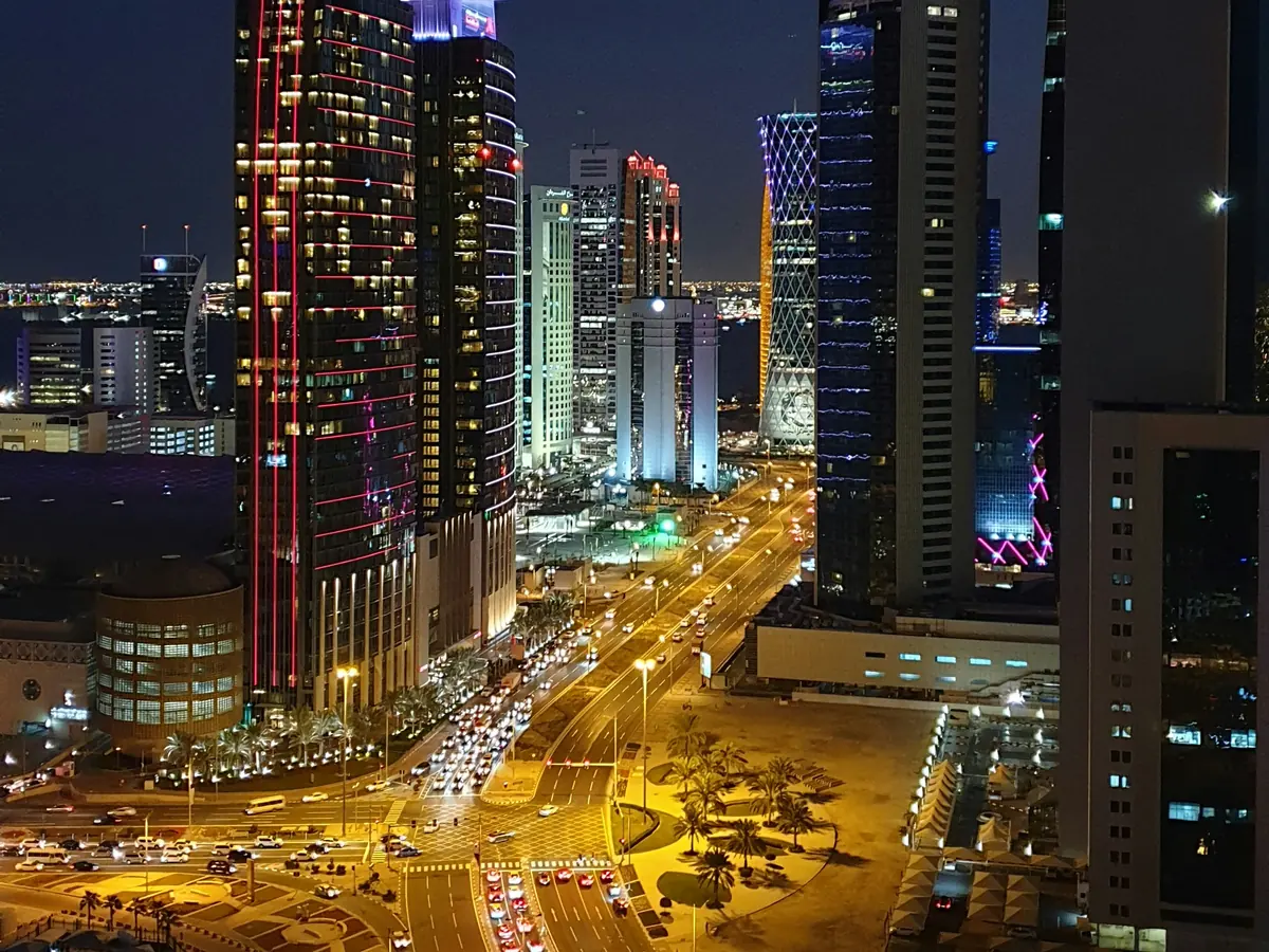 Night view of traffic on wide roads between lit high-rise towers in Doha, seen from Amwal Tower