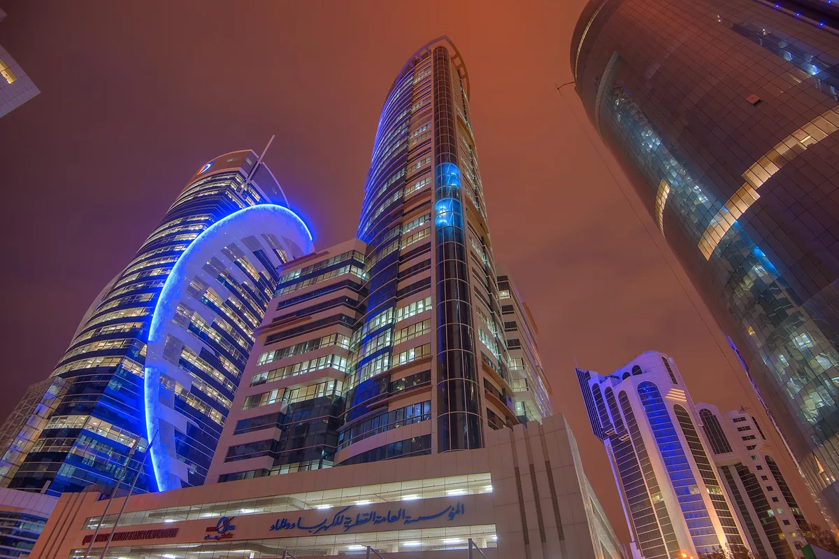 KAHRAMAA headquarters tower in Doha lit at night, with the Qatar General Electricity and Water Corporation sign at street level