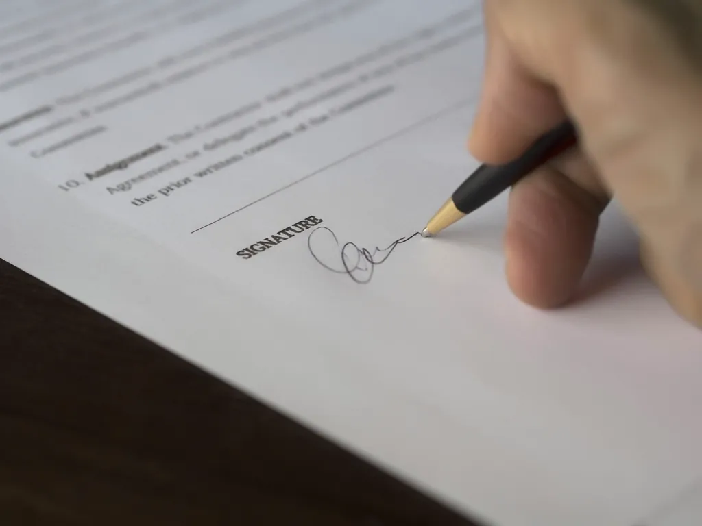 A hand signing a printed contract on the signature line