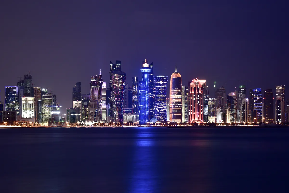 Doha West Bay office towers lit up at night, reflected in the water of Doha Bay