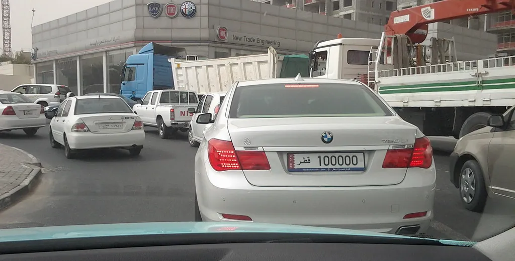 White saloon in Doha traffic with a Qatar private number plate showing the plate number and the word Qatar in Arabic