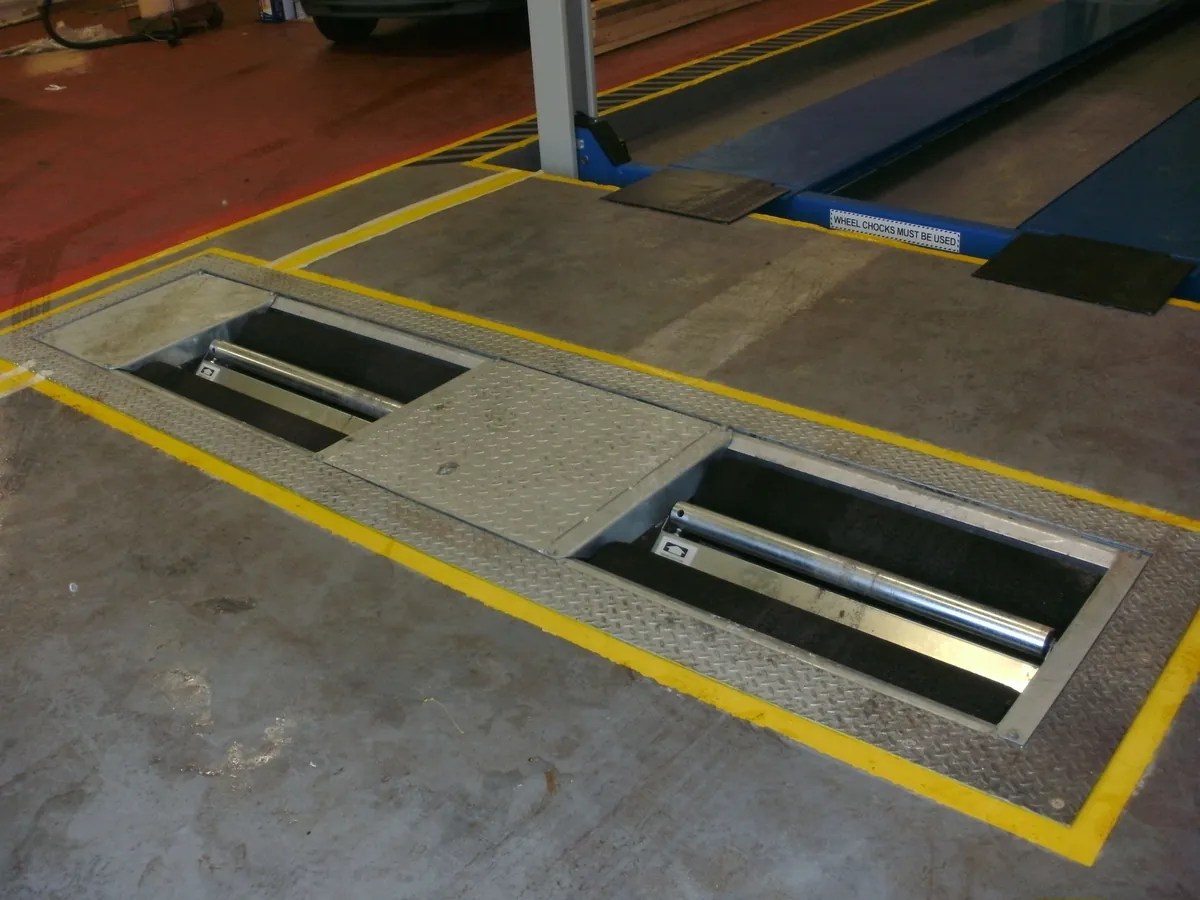 Roller brake tester set into the floor of a vehicle inspection lane, with two pairs of rollers inside yellow-marked pits