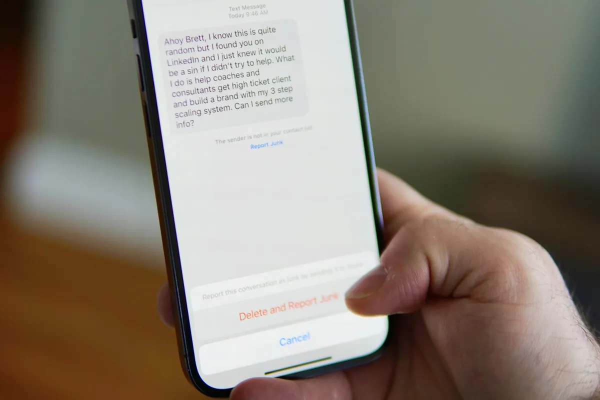 Hand holding a smartphone showing an unsolicited text message with a Delete and Report Junk option