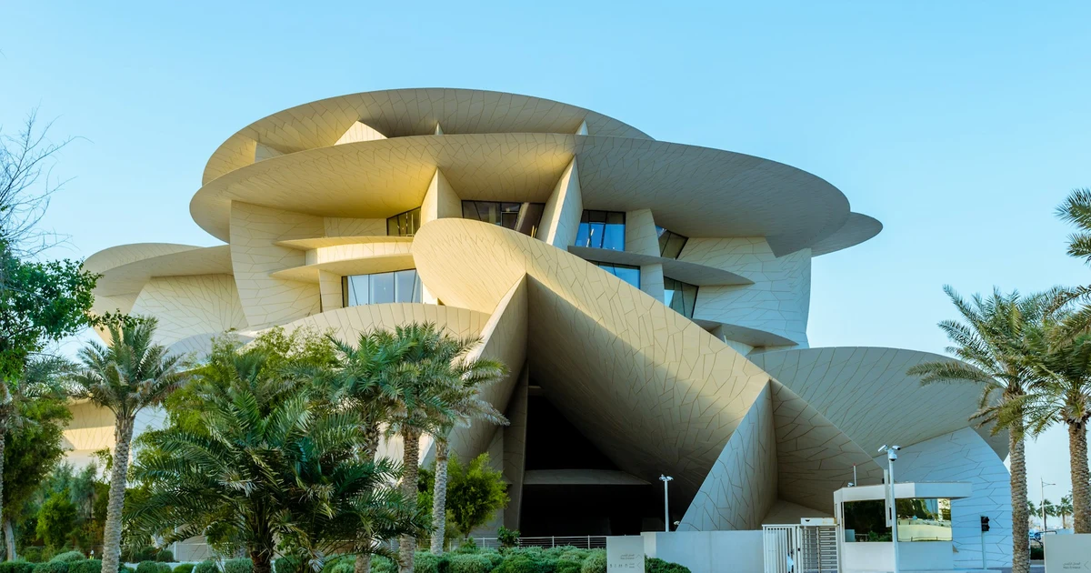 The National Museum of Qatar seen from the landscaped park with palm trees in front of the disc-shaped building