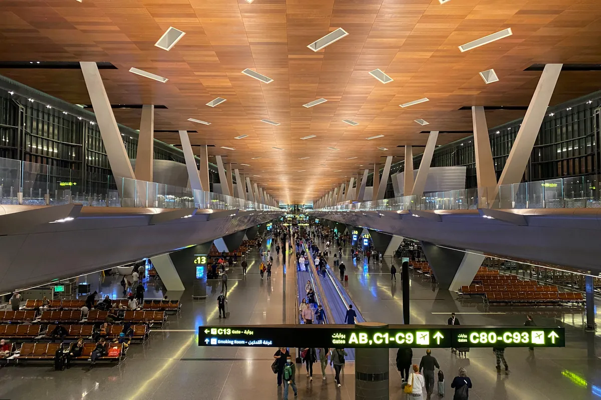 A long departure concourse at Hamad International Airport with a wooden ceiling, seating areas and an overhead sign pointing to gates A, B and C