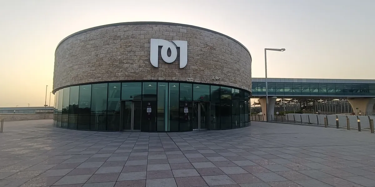 The round stone-clad entrance building of the Hamad International Airport metro station, marked with the Doha Metro logo, at dusk