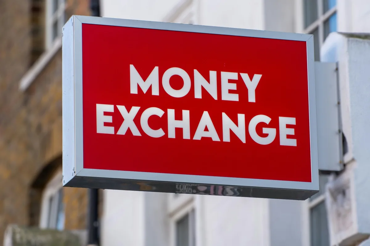 A red Money Exchange shop sign mounted above a street, illustrating the exchange-house channel compared in this guide. Photo not taken in Qatar.