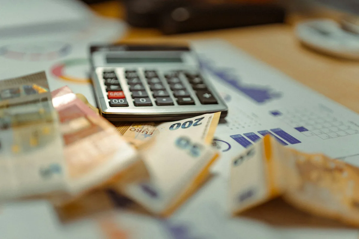 A calculator resting on banknotes and printed financial charts, illustrating how the fee and the exchange rate combine into the total transfer cost.