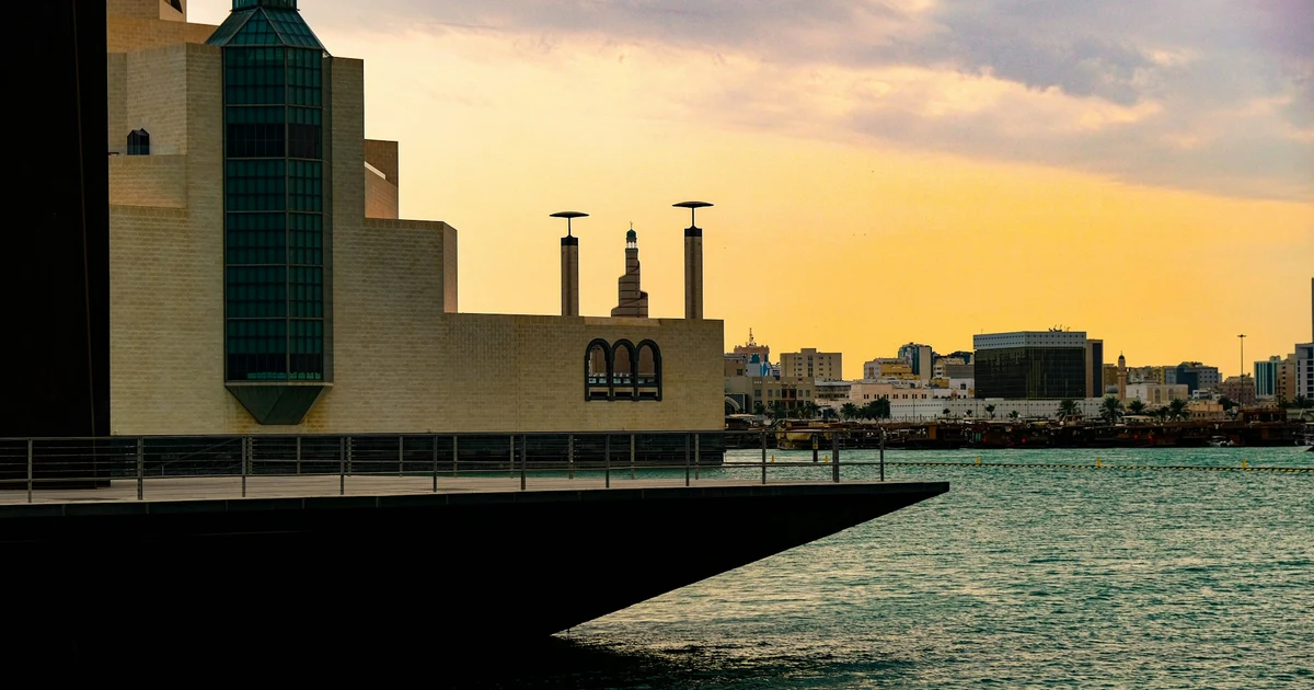 Sunset over Doha Bay seen from the waterfront of the Museum of Islamic Art, with the Corniche skyline in the distance