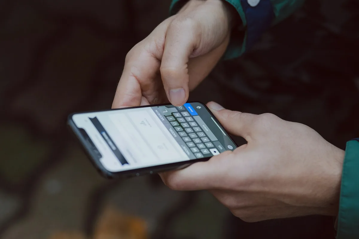 A person holding a smartphone in both hands and typing on the on-screen keyboard, illustrating the app route for sending money.