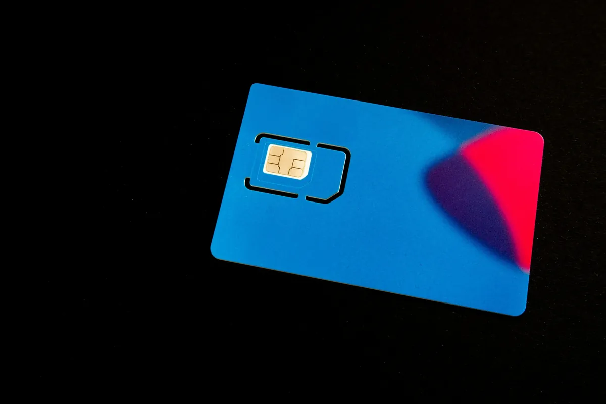 A blue SIM card with a gold chip on a dark surface, illustrating the mobile number linked to a Tawtheeq account