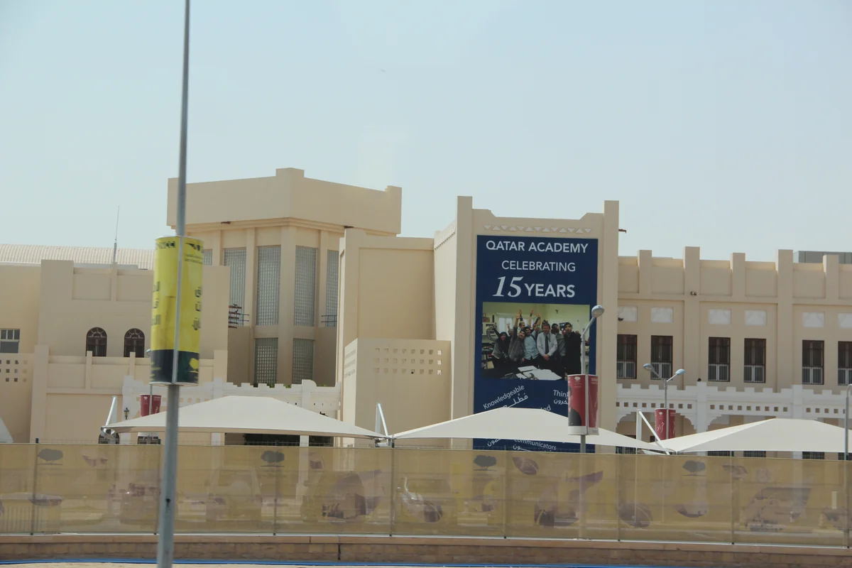 Sand-colored Qatar Academy school building in Al Rayyan, Qatar, with a large banner reading Qatar Academy Celebrating 15 Years