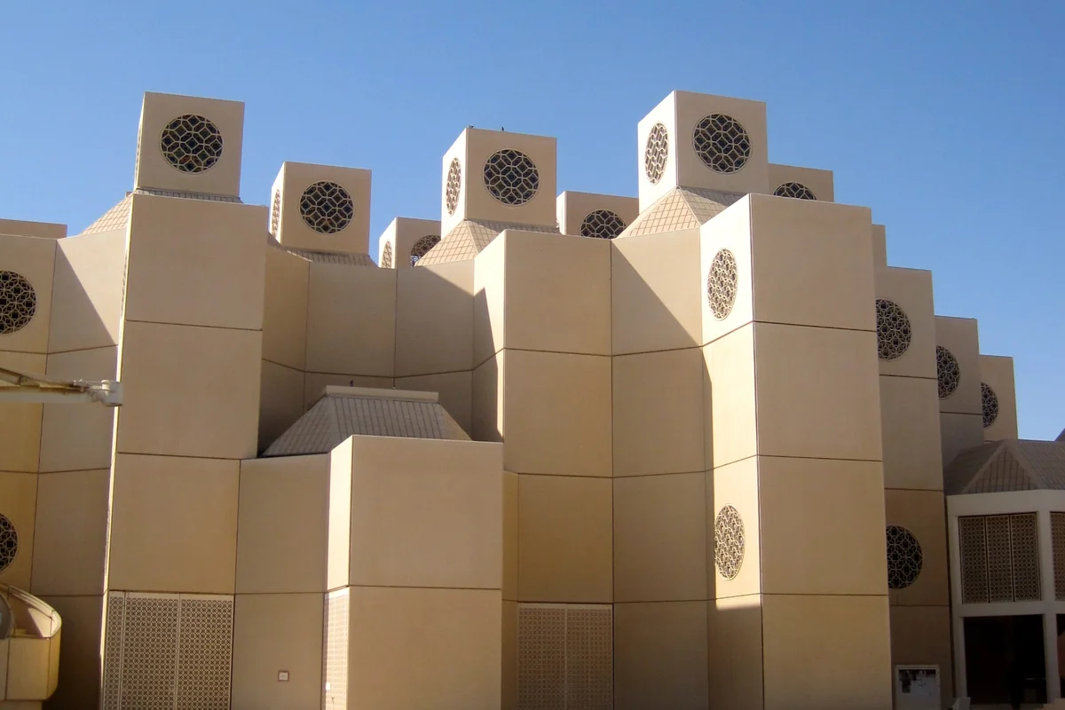 Beige campus buildings at Qatar University topped with square wind towers with round lattice openings, against a clear blue sky